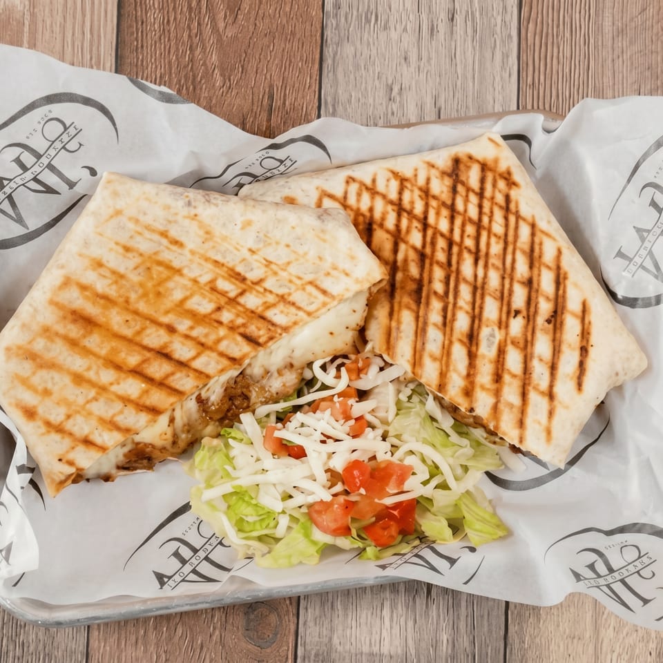 Two grilled wraps with melted cheese and meat, served with a side salad on branded paper.