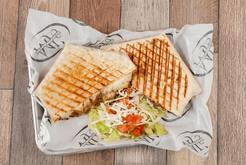 Two grilled wraps with melted cheese and meat, served with a side salad on branded paper.