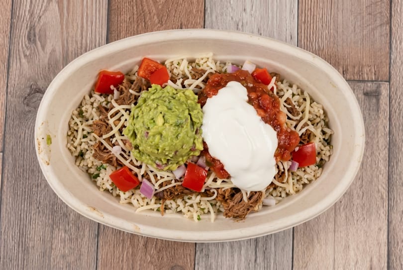 Burrito bowl with shredded beef, rice, cheese, guacamole, salsa, sour cream, and diced tomatoes.
