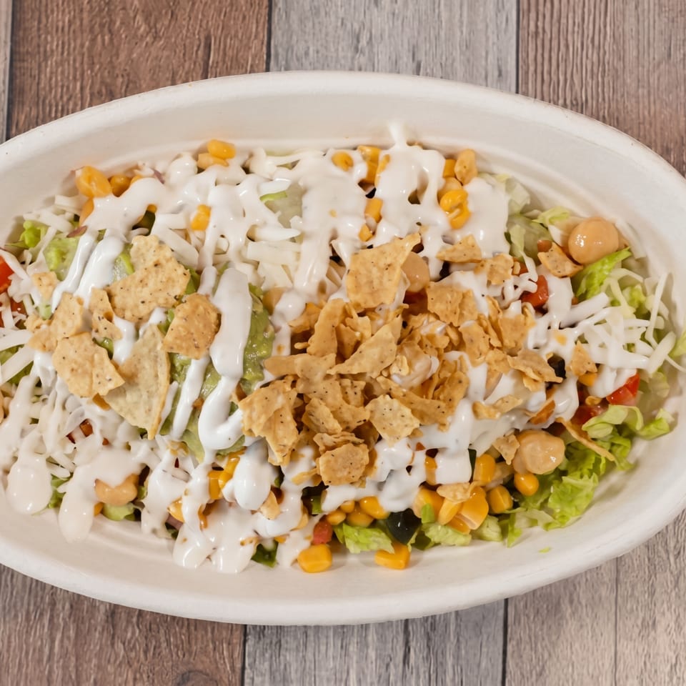 Overhead view of a salad bowl with lettuce, corn, cheese, tortilla chips, and white dressing.