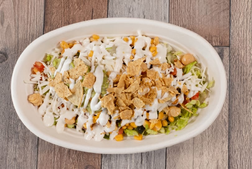 Overhead view of a salad bowl with lettuce, corn, cheese, tortilla chips, and white dressing.